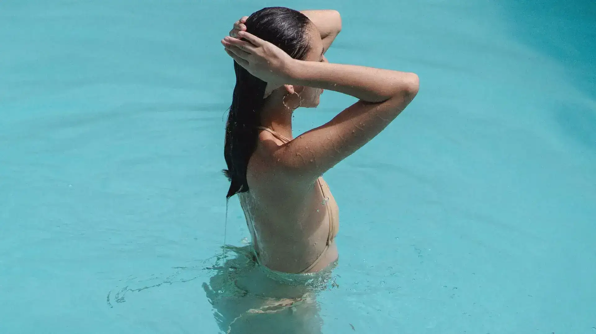 Woman with wet hair standing in a turquoise swimming pool.
