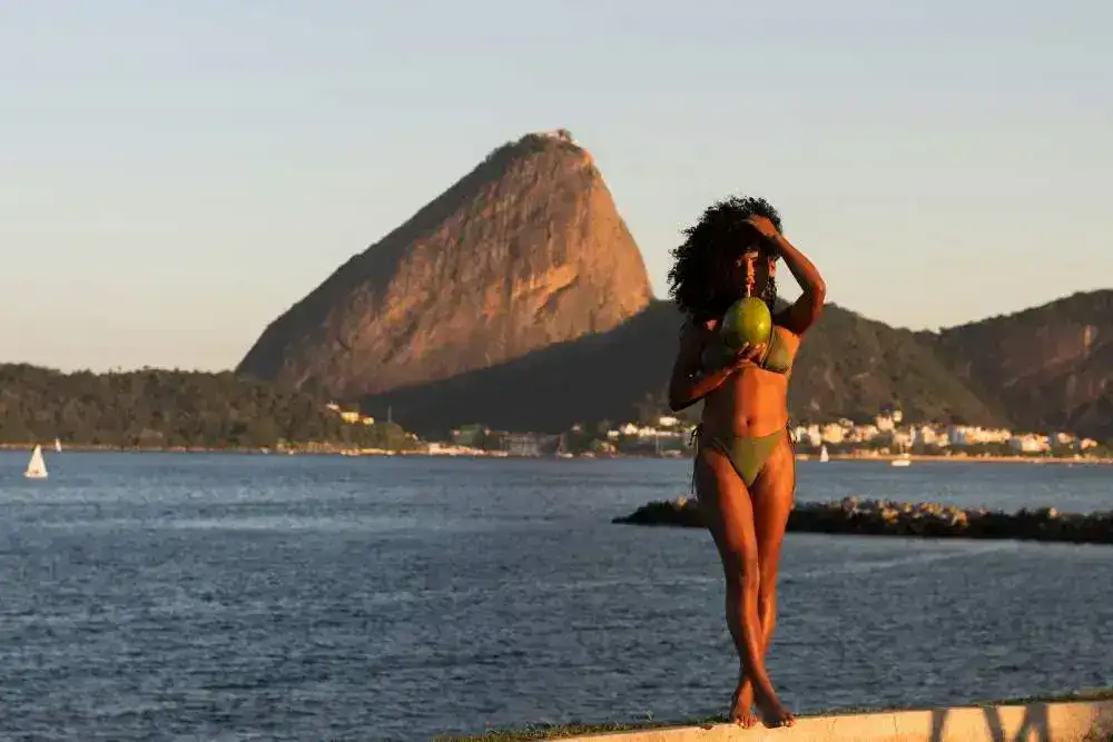 Woman in bikini drinking coconut near Sugarloaf Mountain, Brazil.