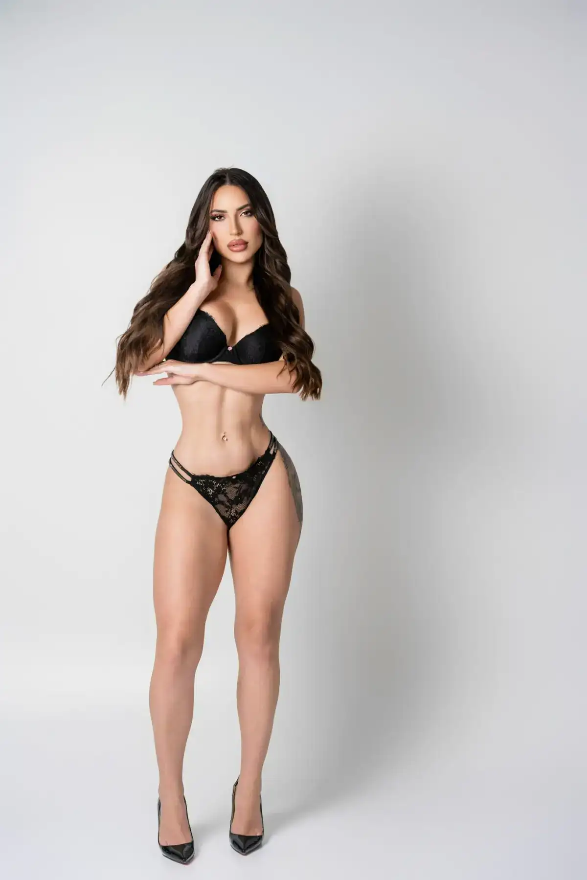 Woman in black lace lingerie posing against white background.