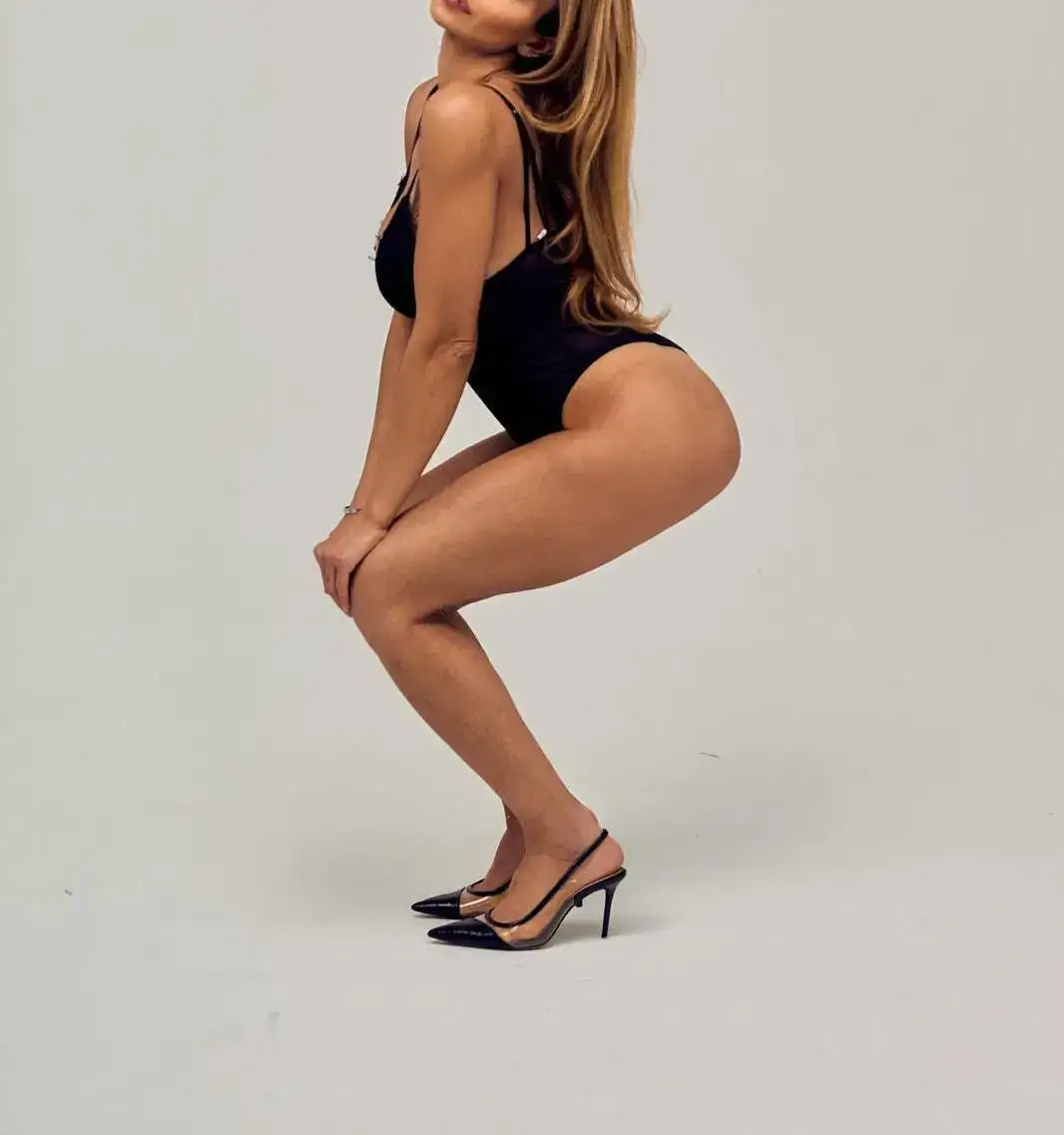 Woman posing in a black bodysuit and slingback heels.