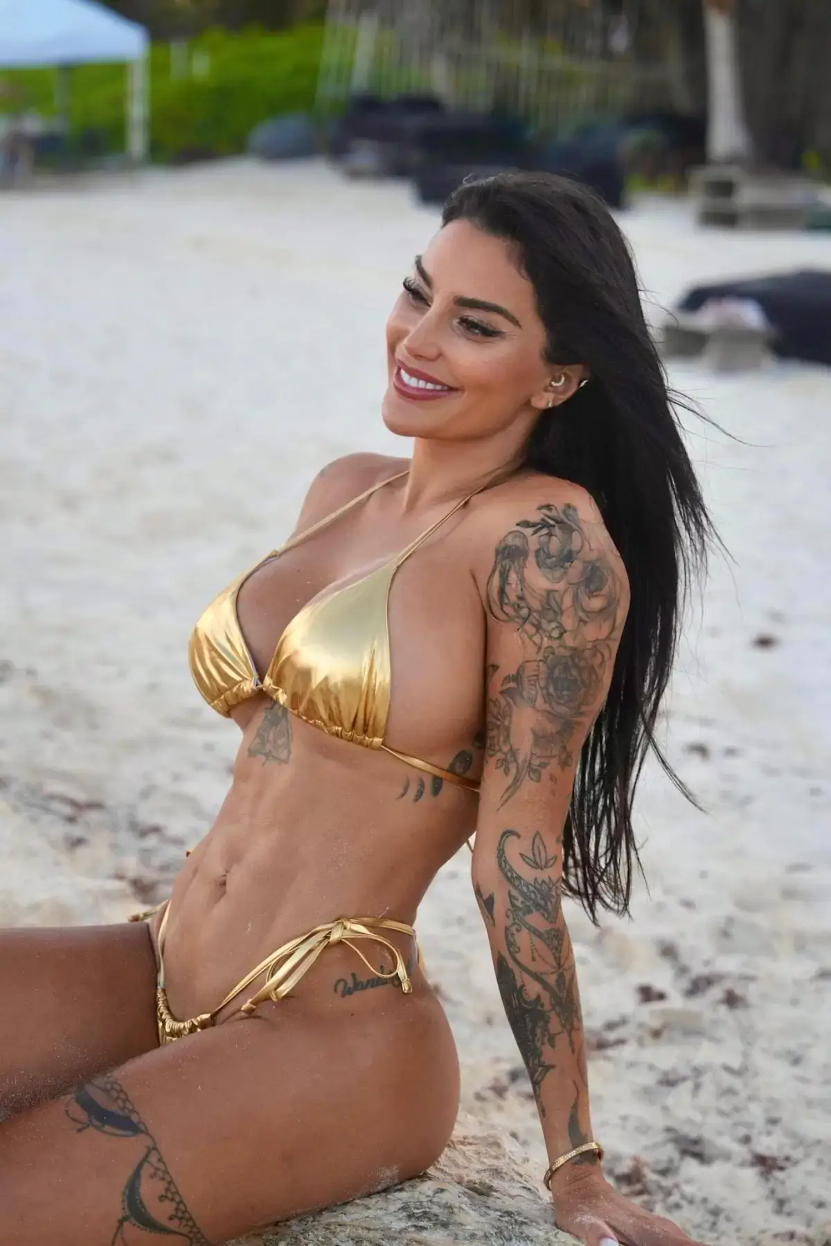 Woman with tattoos in a gold bikini on the beach.